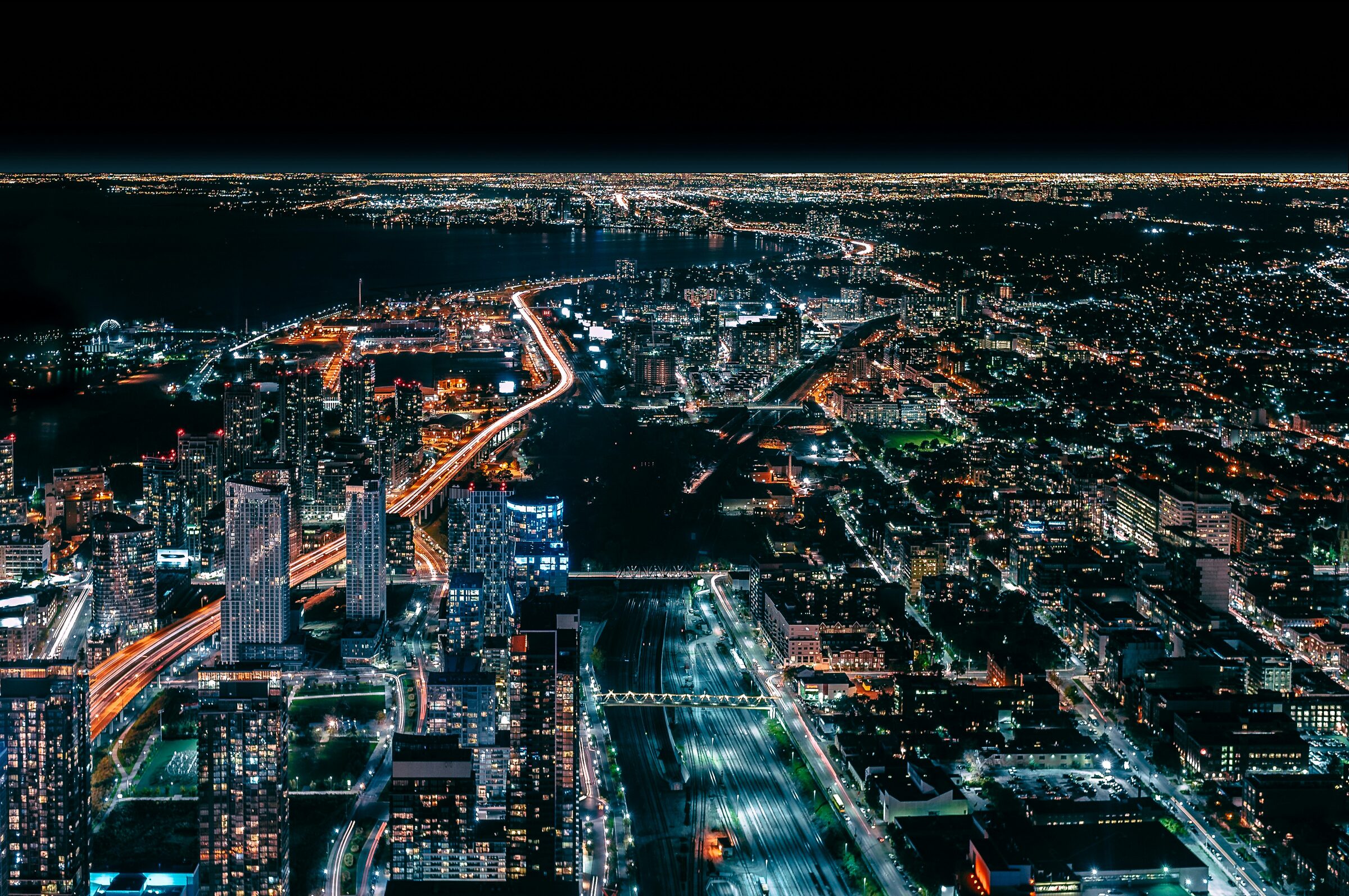 A city at night seen from above, lit highways running out to the horizon