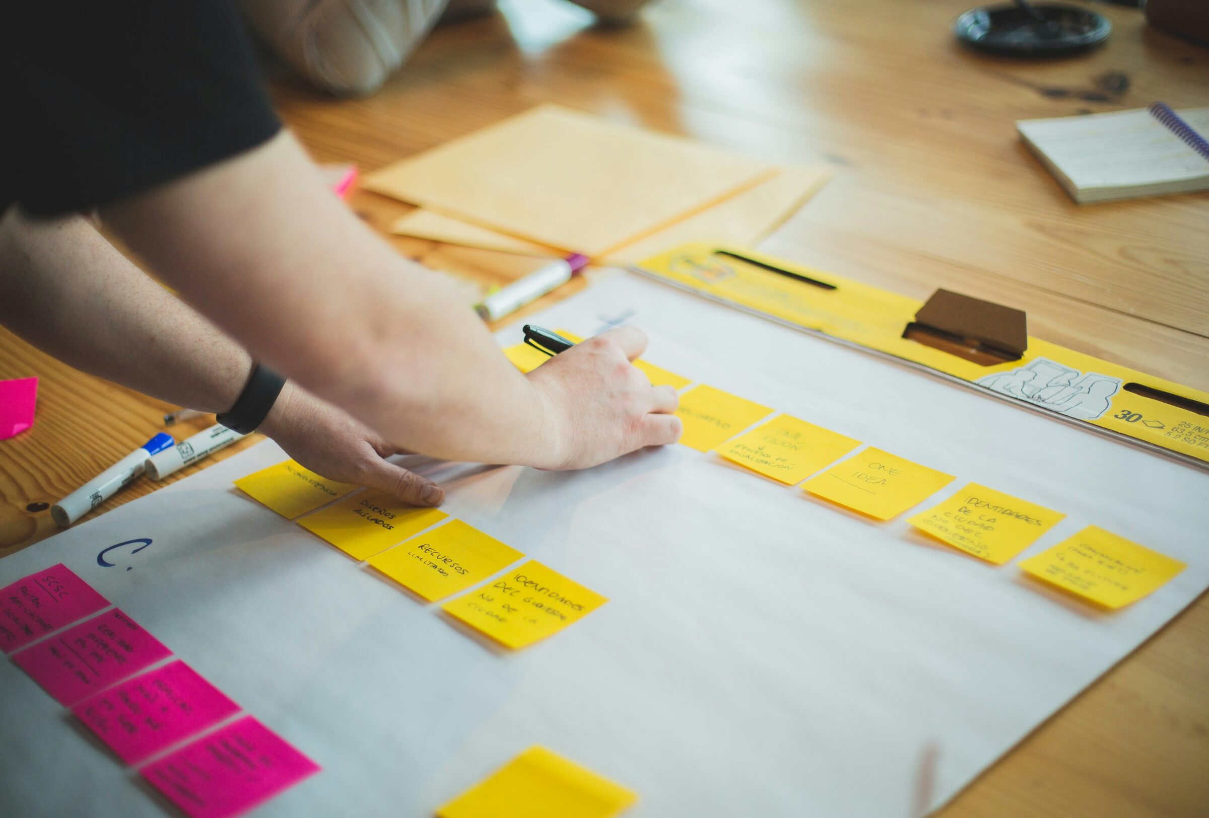 Hands arranging yellow and pink sticky notes across a planning sheet