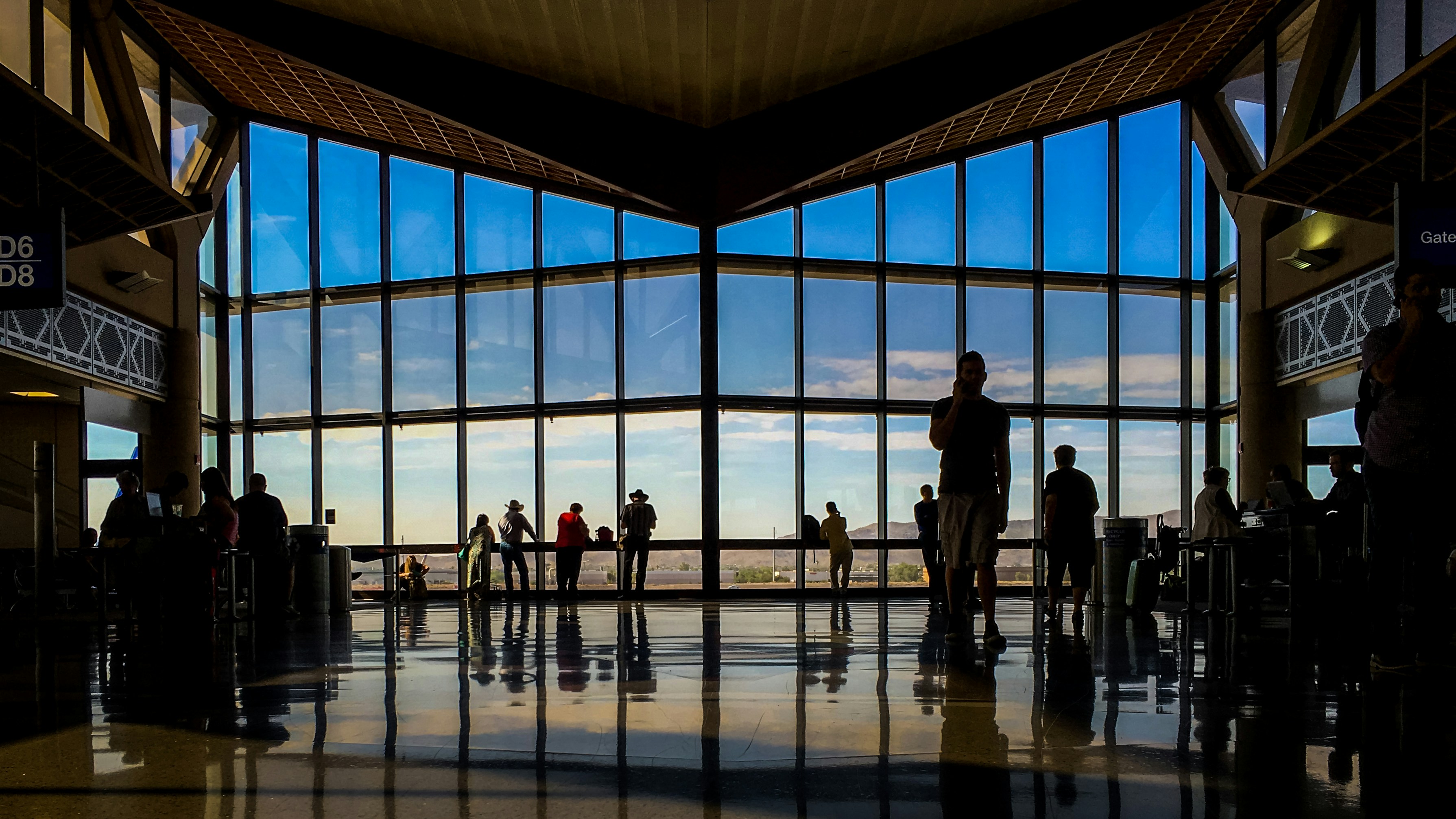 Travelers silhouetted against the floor-to-ceiling windows of a sunlit airport terminal