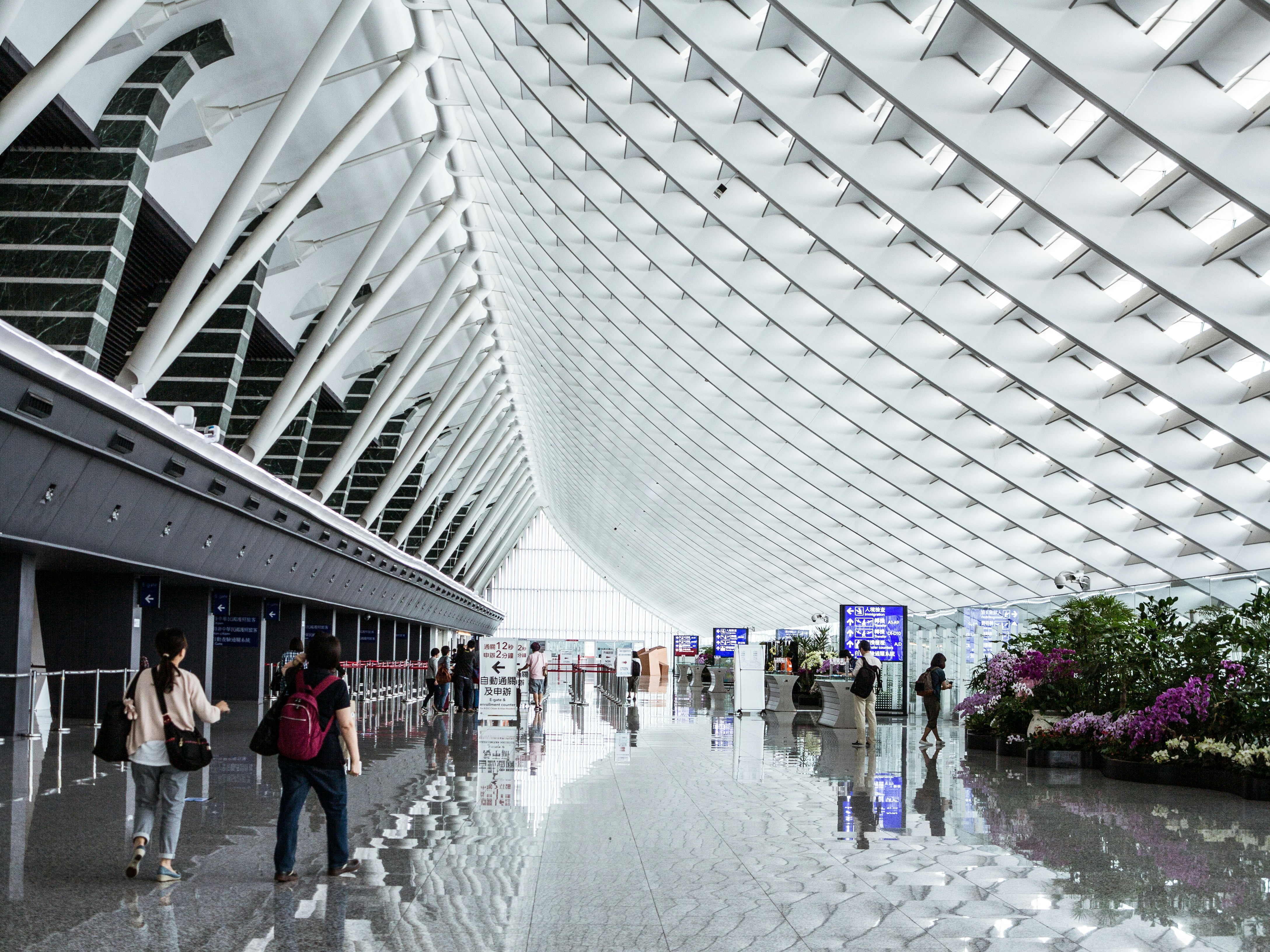 Bright airport concourse under a ribbed white roof with travelers walking